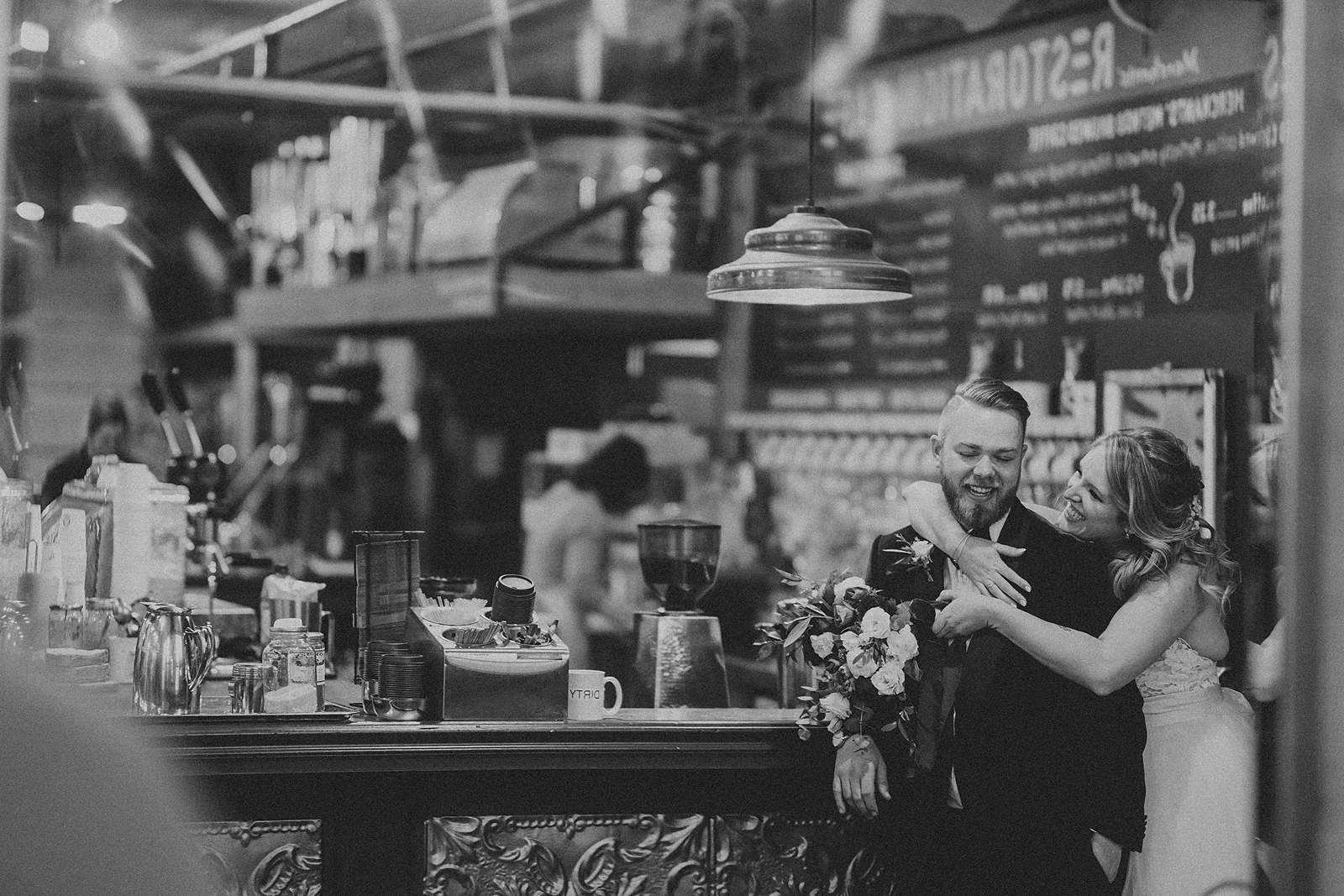 A bride hugs her groom in front of the coffee counter at the Merchants of Green Coffee in Toronto