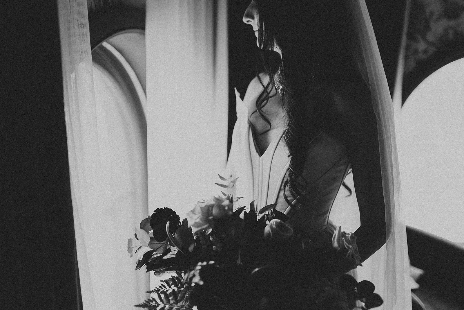 a black and white photo of a bride by a window