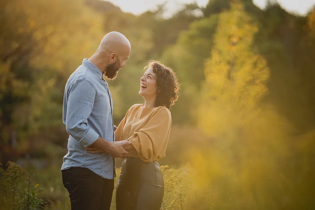 An engaged couple laughing surrounded by fall colours in Toronto