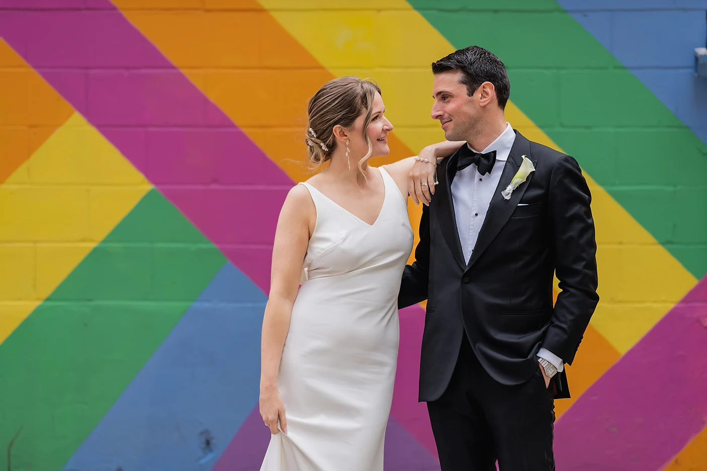 The bride and groom stand inn front of a colourful wall near Ricarda's