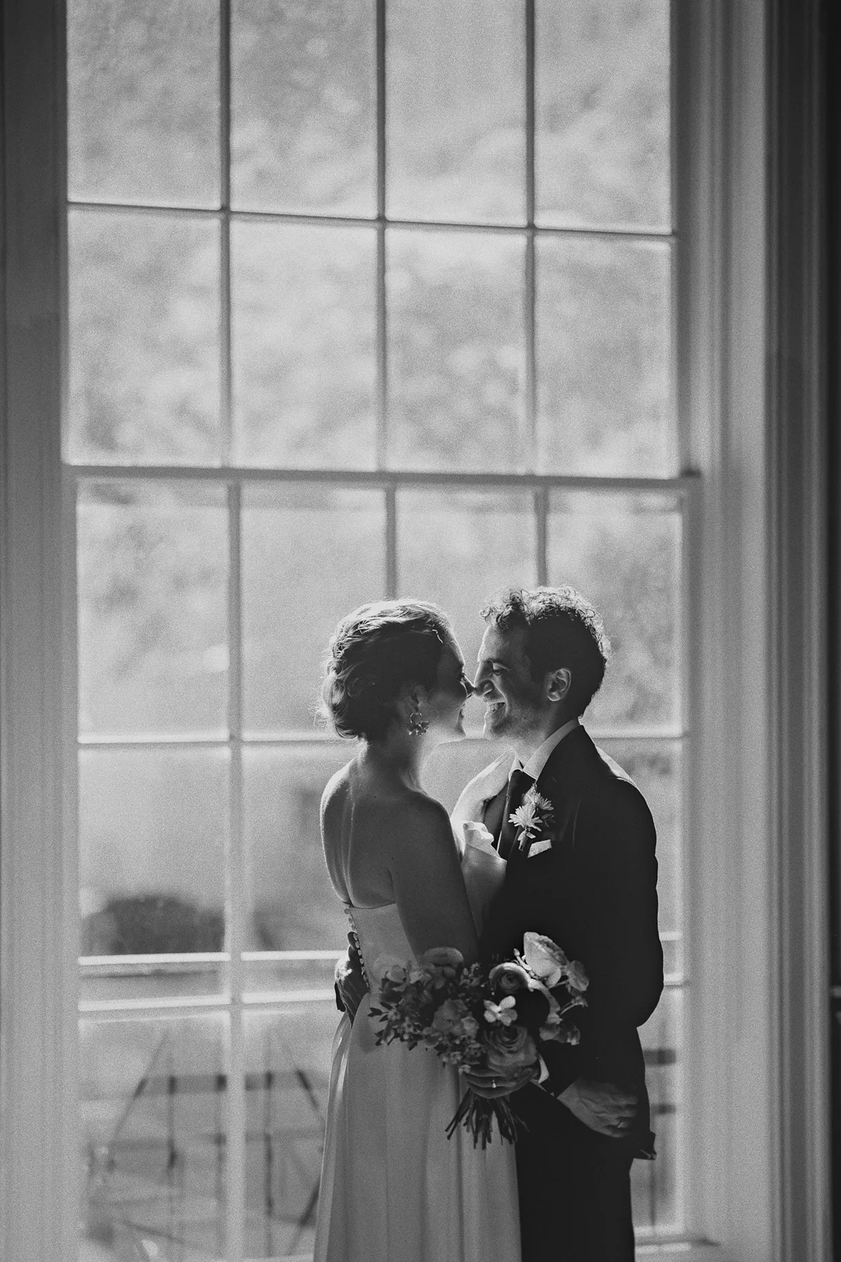 The couple kisses in front of a bright window