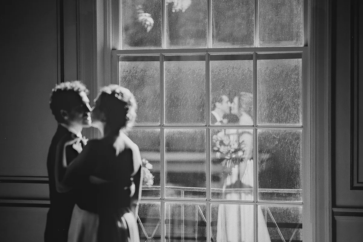 The couple kisses, reflected in the window pane