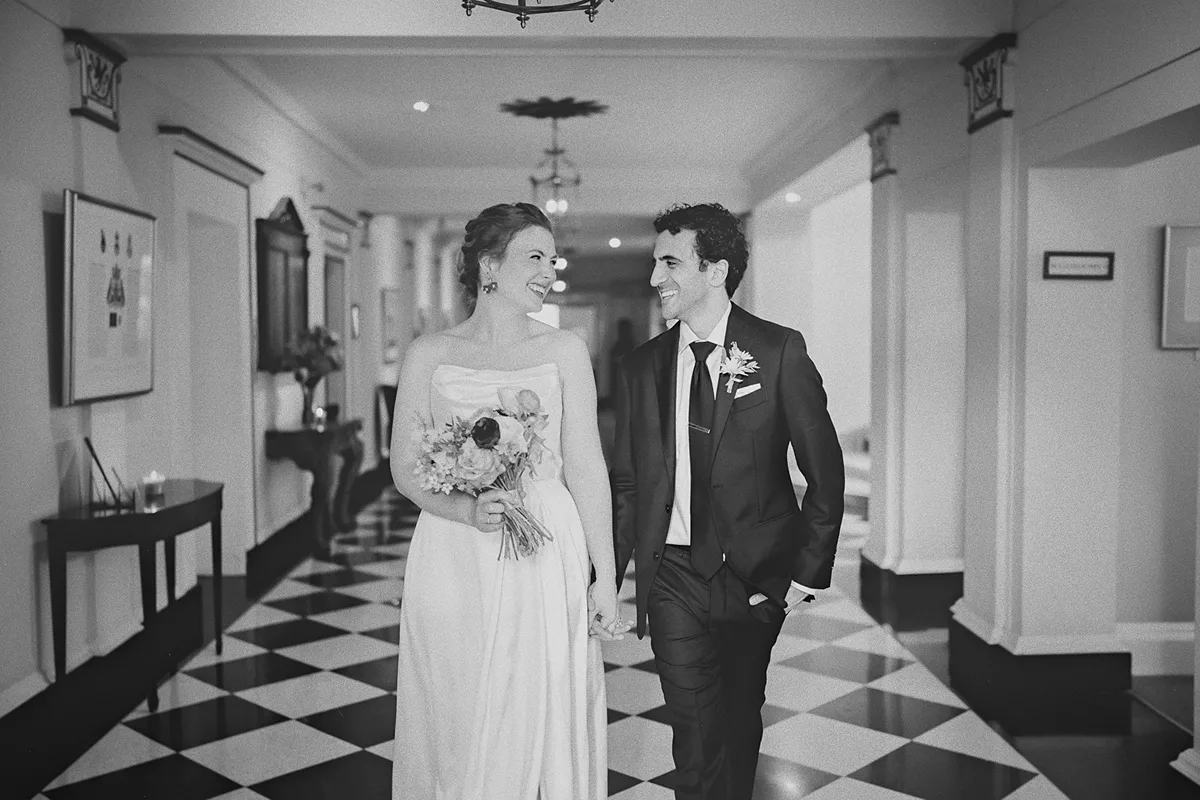 The couple smiles at each other in a University Club hallway