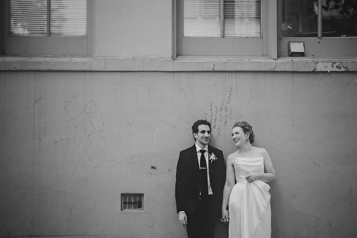 A wide, creative portrait of the couple against a wall
