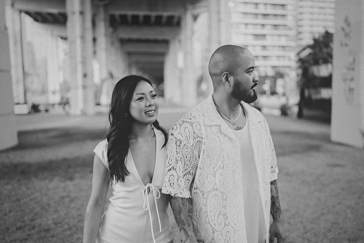 The couple walks hand-in-hand under an overpass.