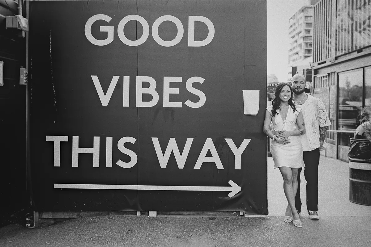 Corrina and Jamie pose next to a 'Good Vibes This Way' sign.