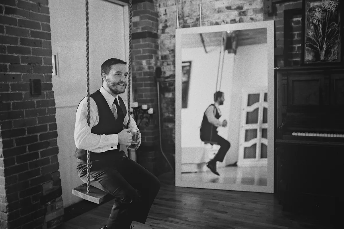 A creative portrait of a groomsman on a swing with a mirror