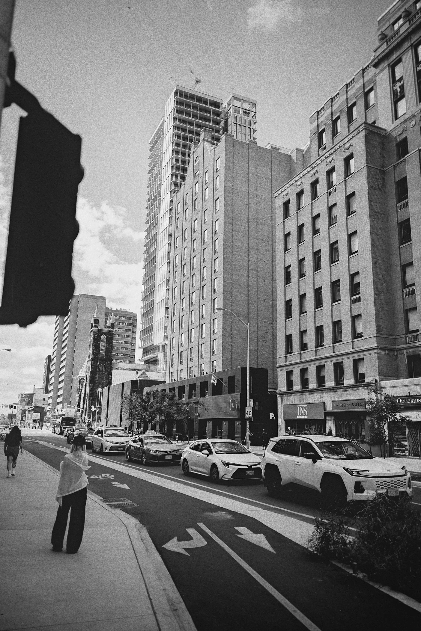 A city street view with tall buildings and cars parked along the curb on a bright day.