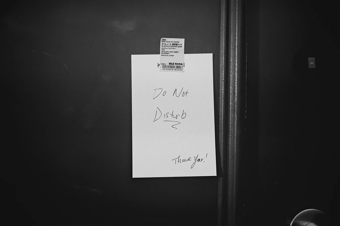 A handwritten "Do Not Disturb" note is taped to a dark hotel room door.