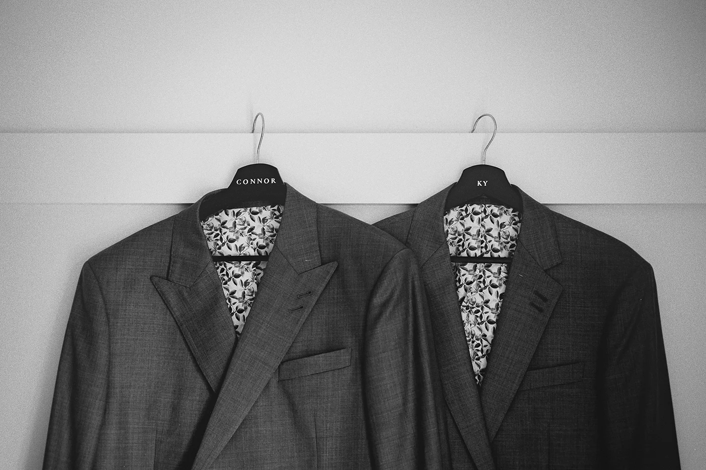 A detailed view of the two wedding suits hanging side-by-side before the ceremony.