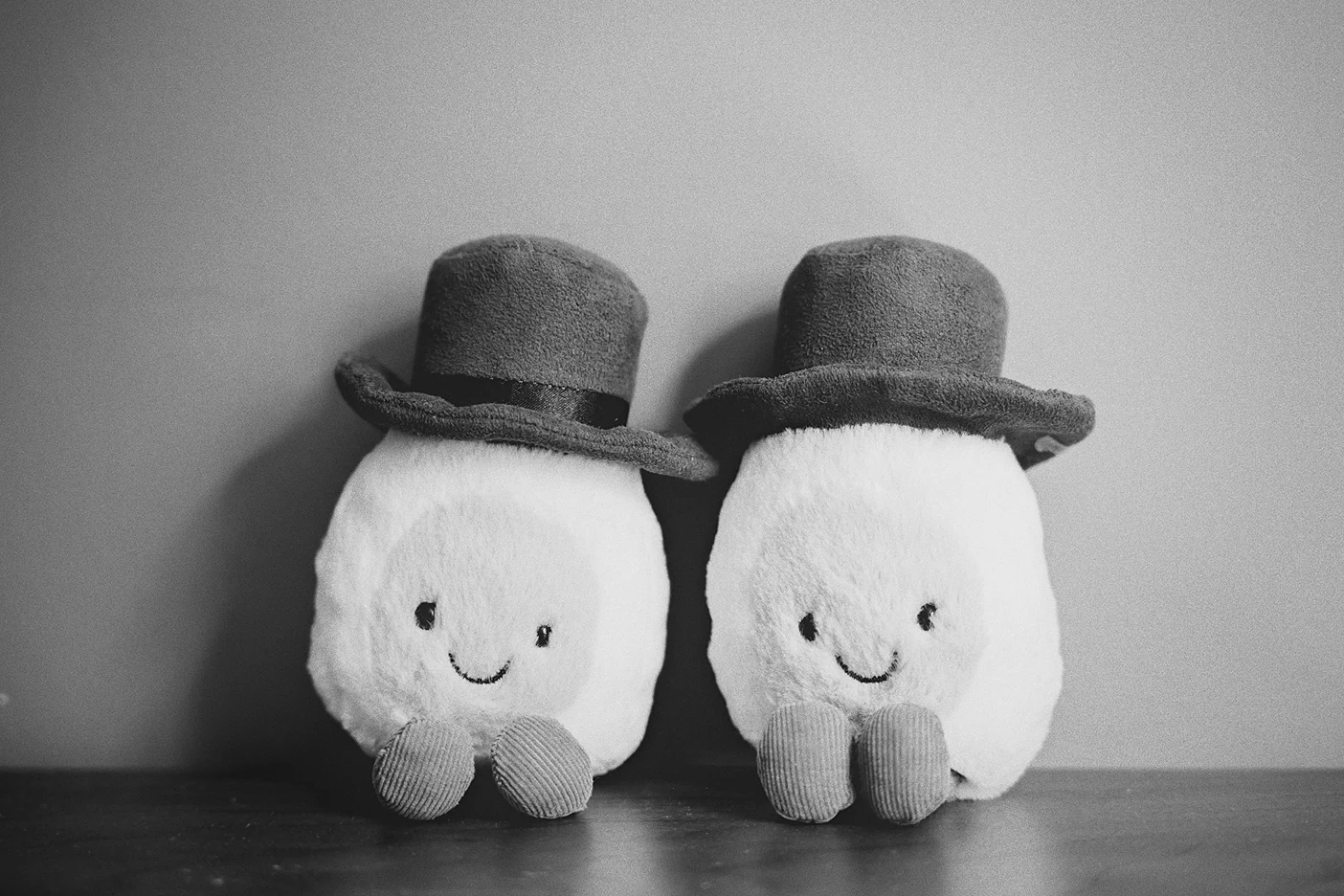 Two whimsical plush toys wearing top hats sit on a wooden surface as wedding decor.