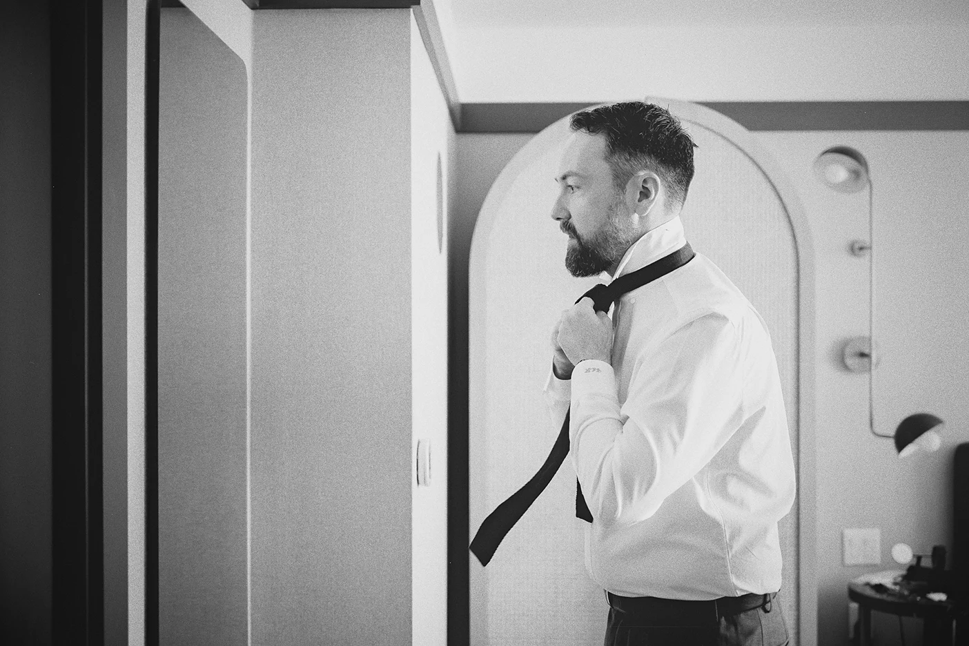Reflected in a mirror, Connor carefully adjusts the knot of his wedding tie.