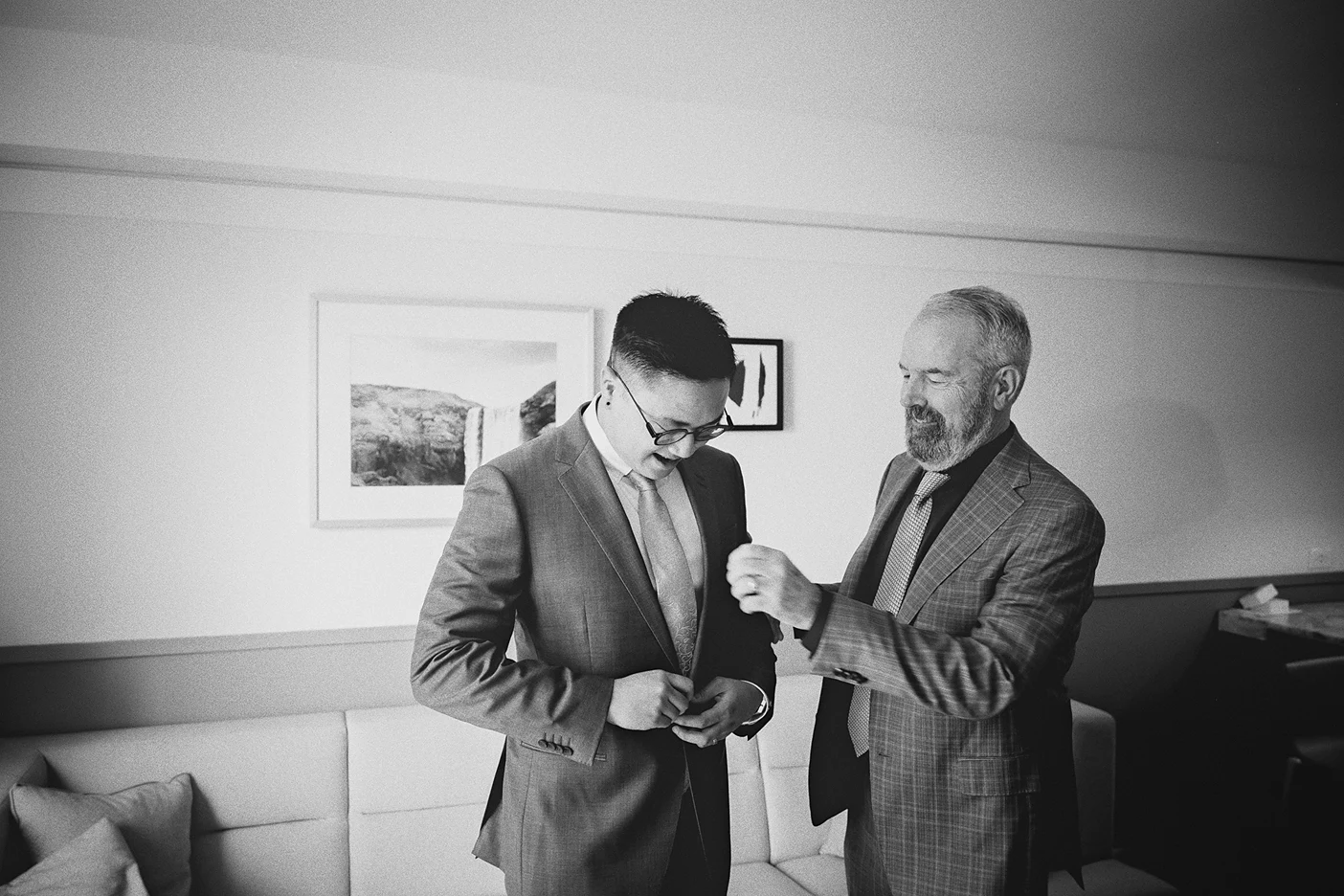 Ky looks down as a guest helps him fasten the buttons on his suit jacket.