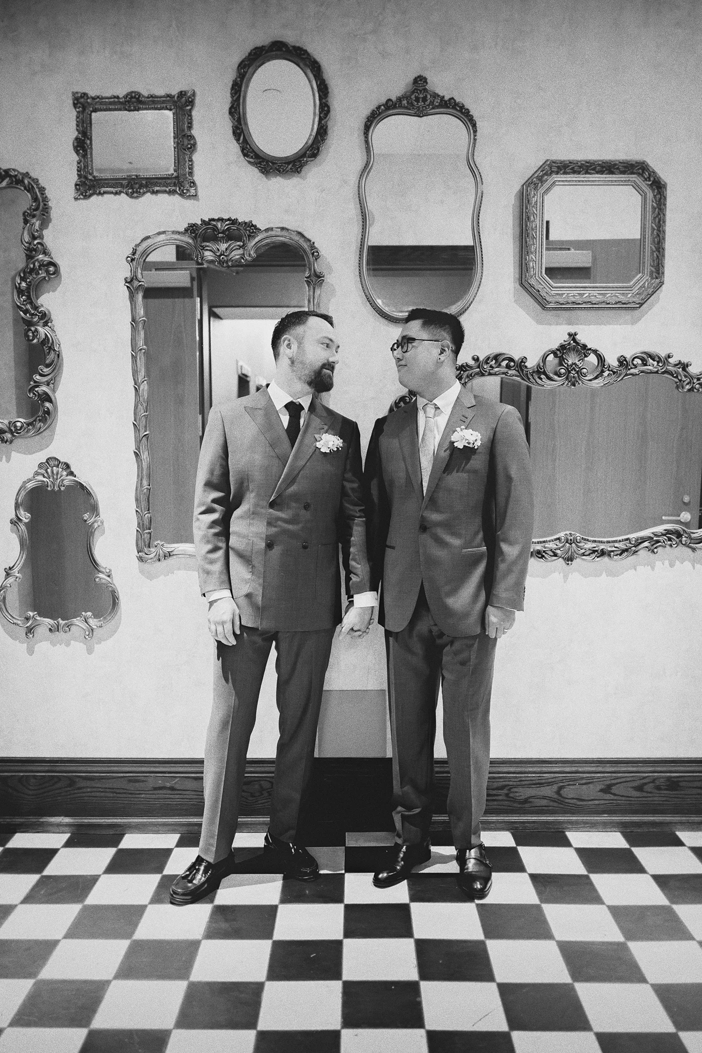 The grooms share a look while standing on a checkered floor in a stylish room.