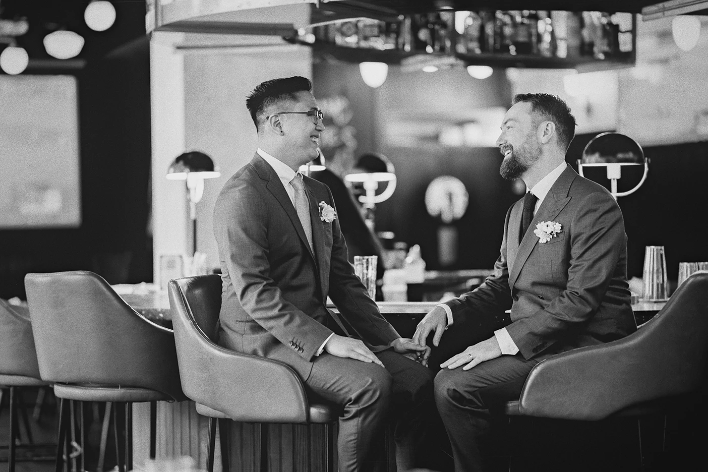 The grooms laugh together during a relaxed moment at the bar before the ceremony.