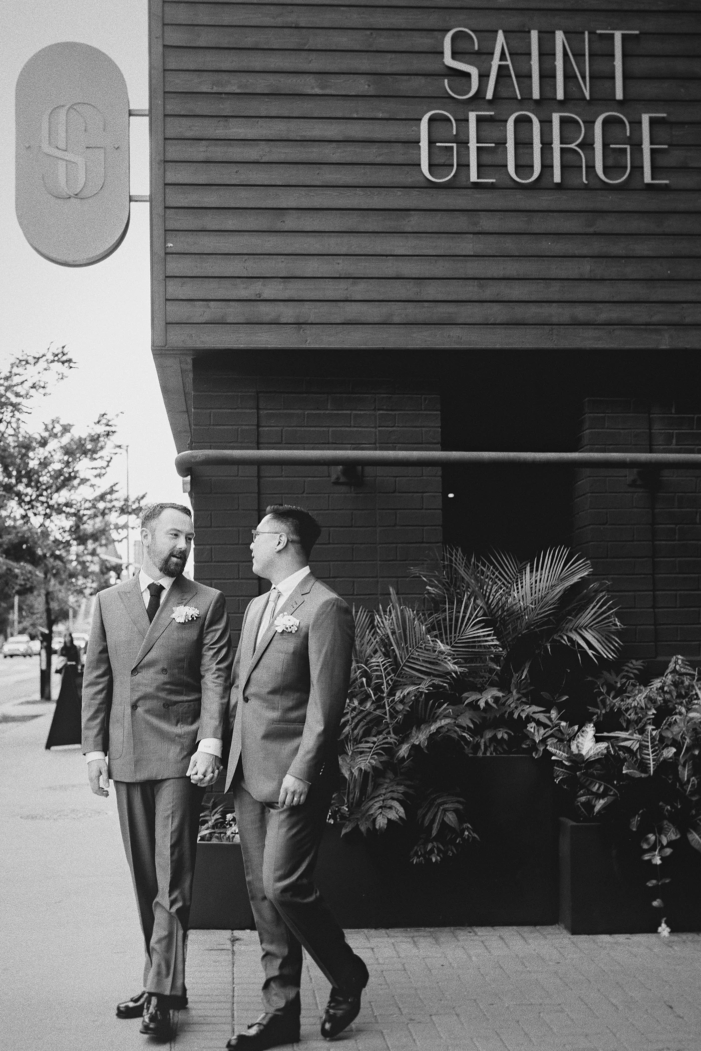 Holding hands, the grooms walk along the sidewalk outside the Saint George hotel.