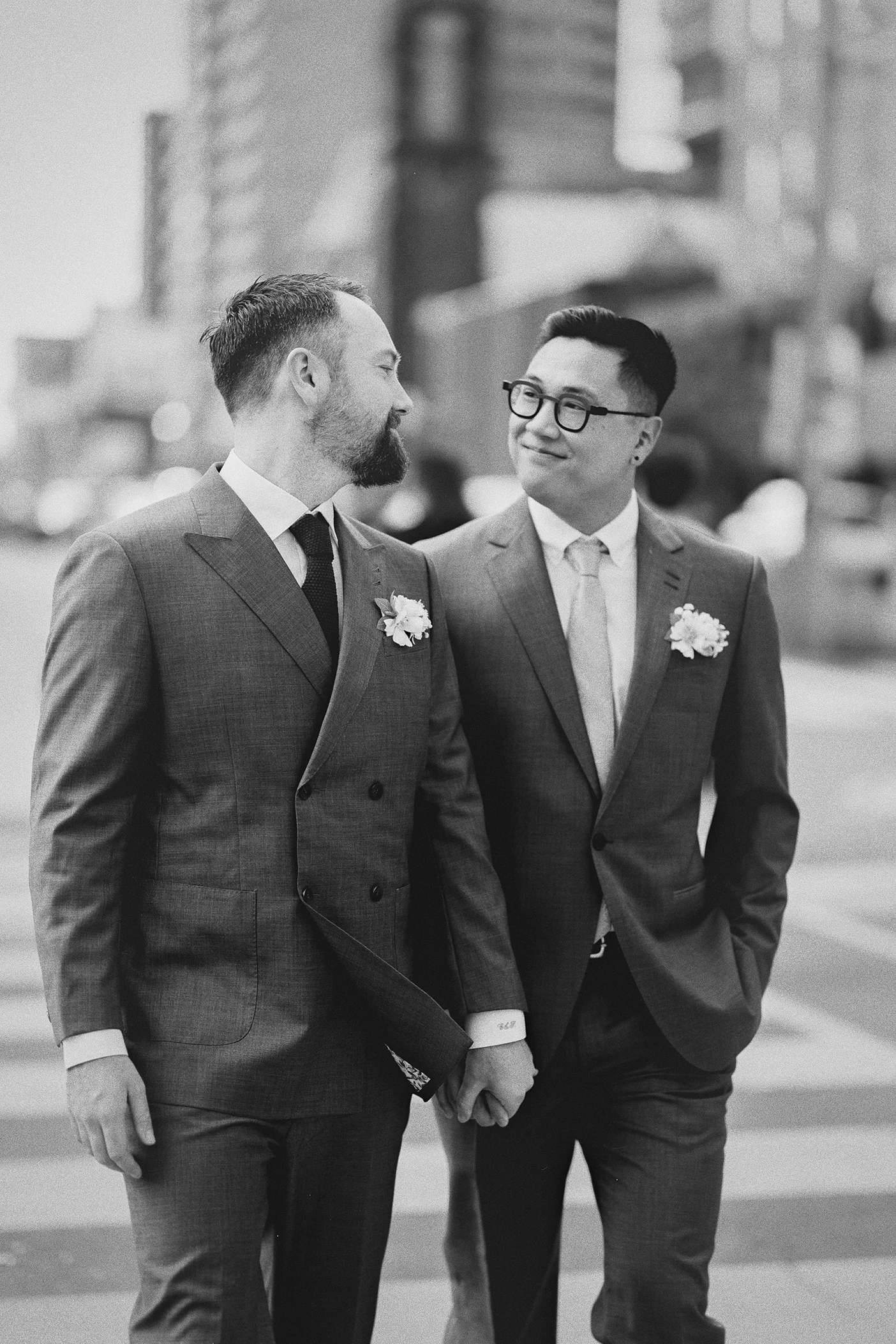 The grooms exchange a happy glance while walking across a city street together.