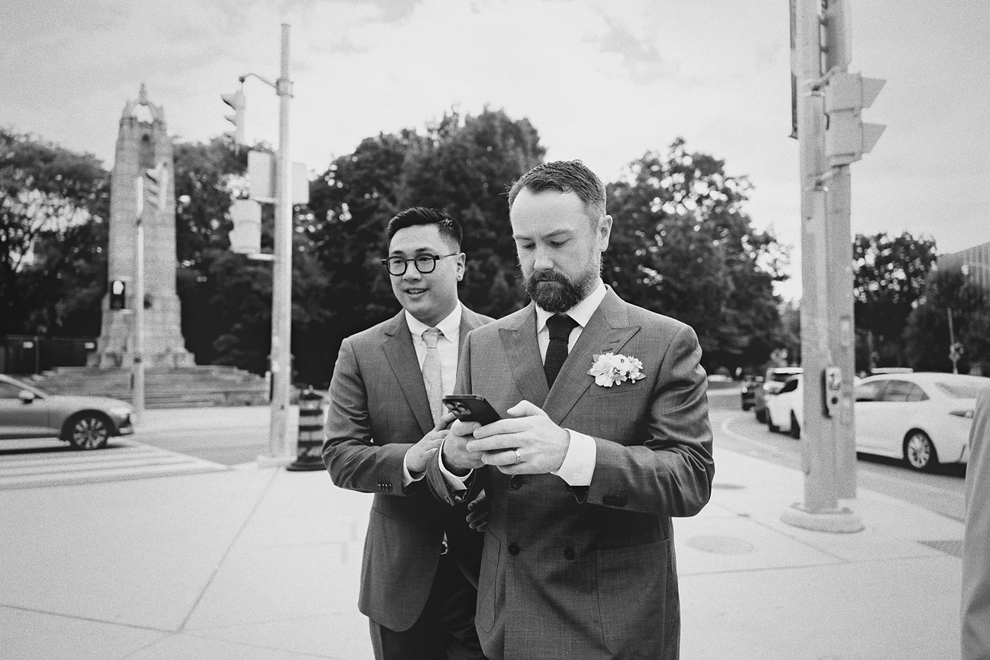 The grooms pause on the sidewalk to look at a phone before the ceremony.
