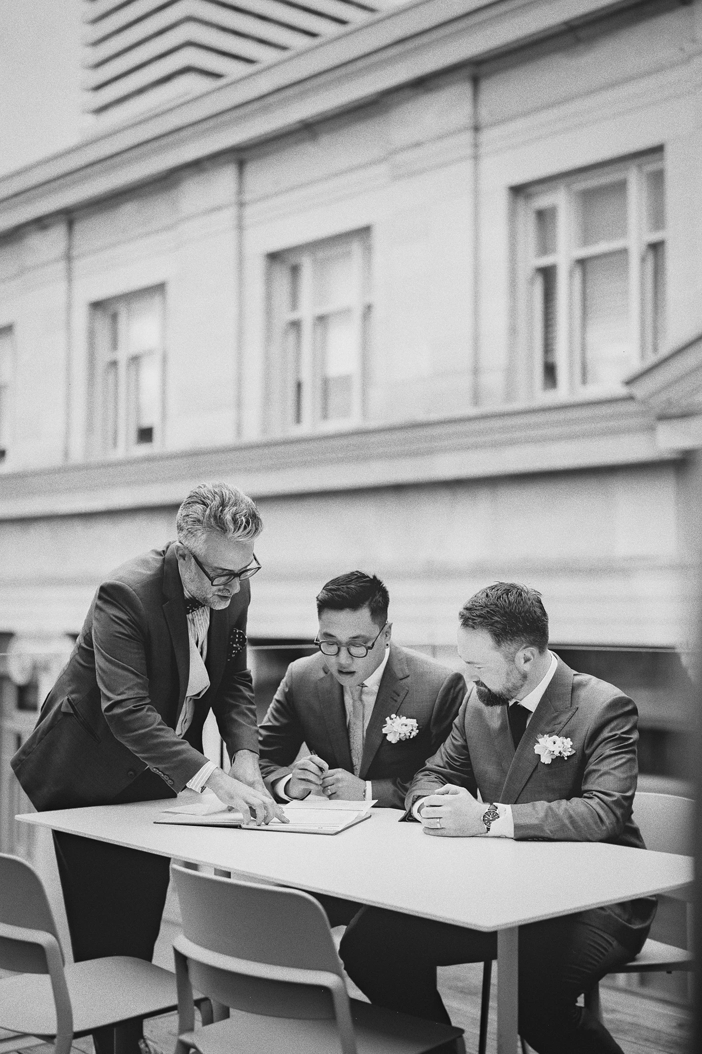 The grooms look on as the officiant points to the signature line.