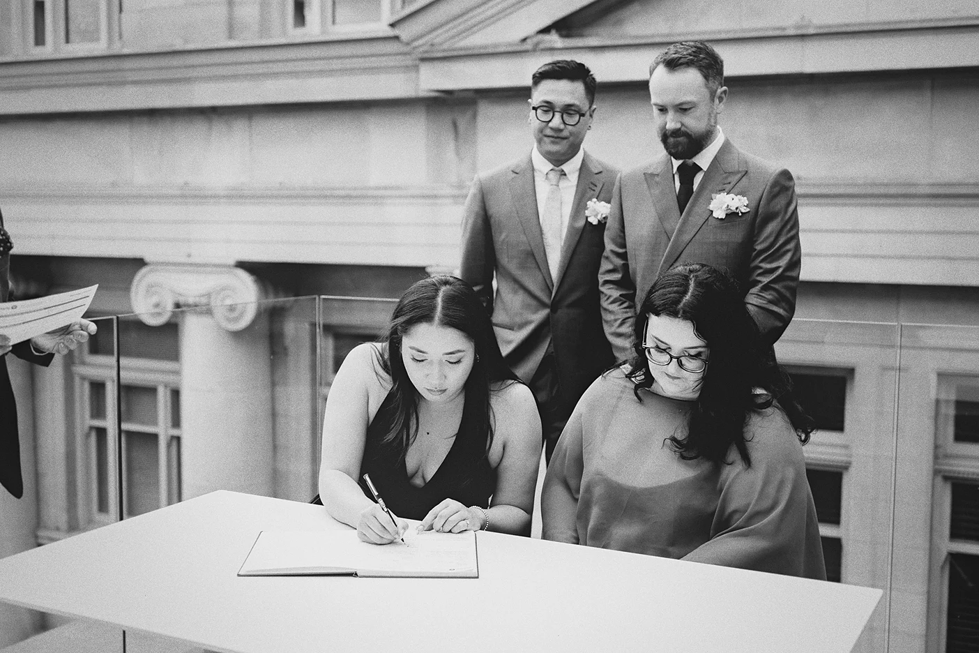 A witness signs the marriage register as the couple stands behind her.