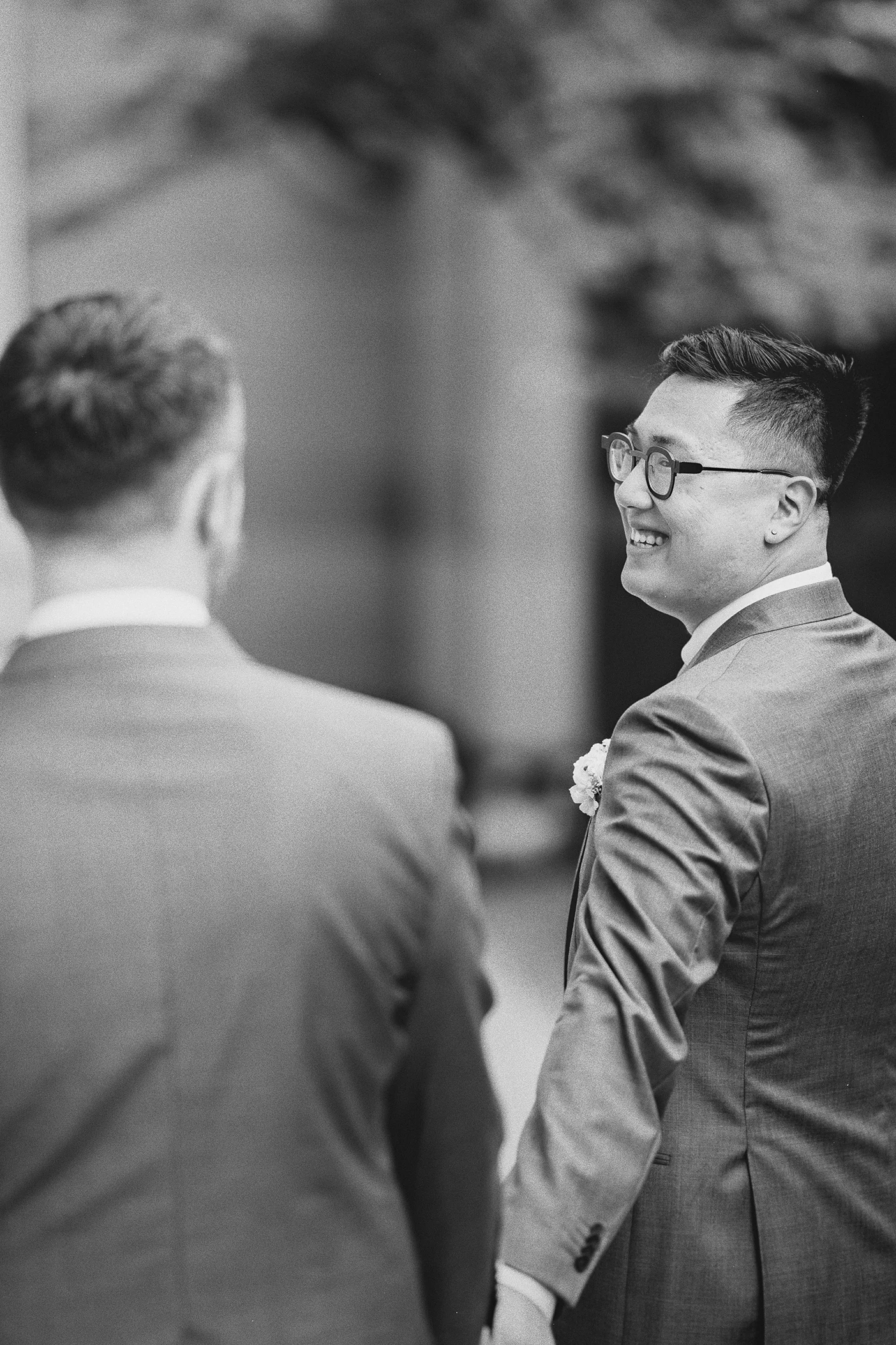 Groom 1 smiles as he looks back at groom 2 while walking.