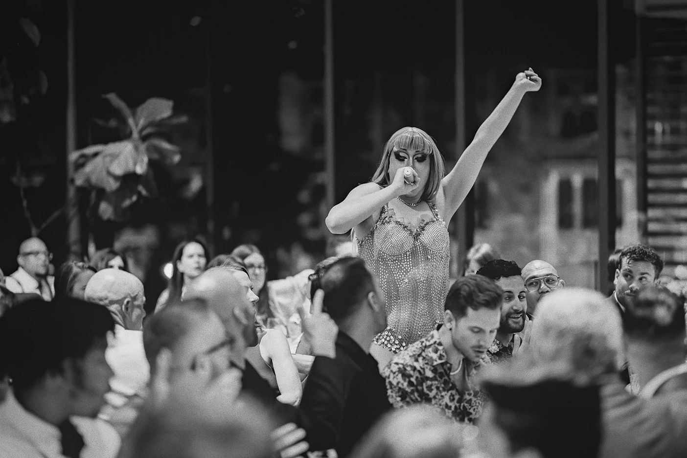 The drag performer stands on a chair to sing to the guests.