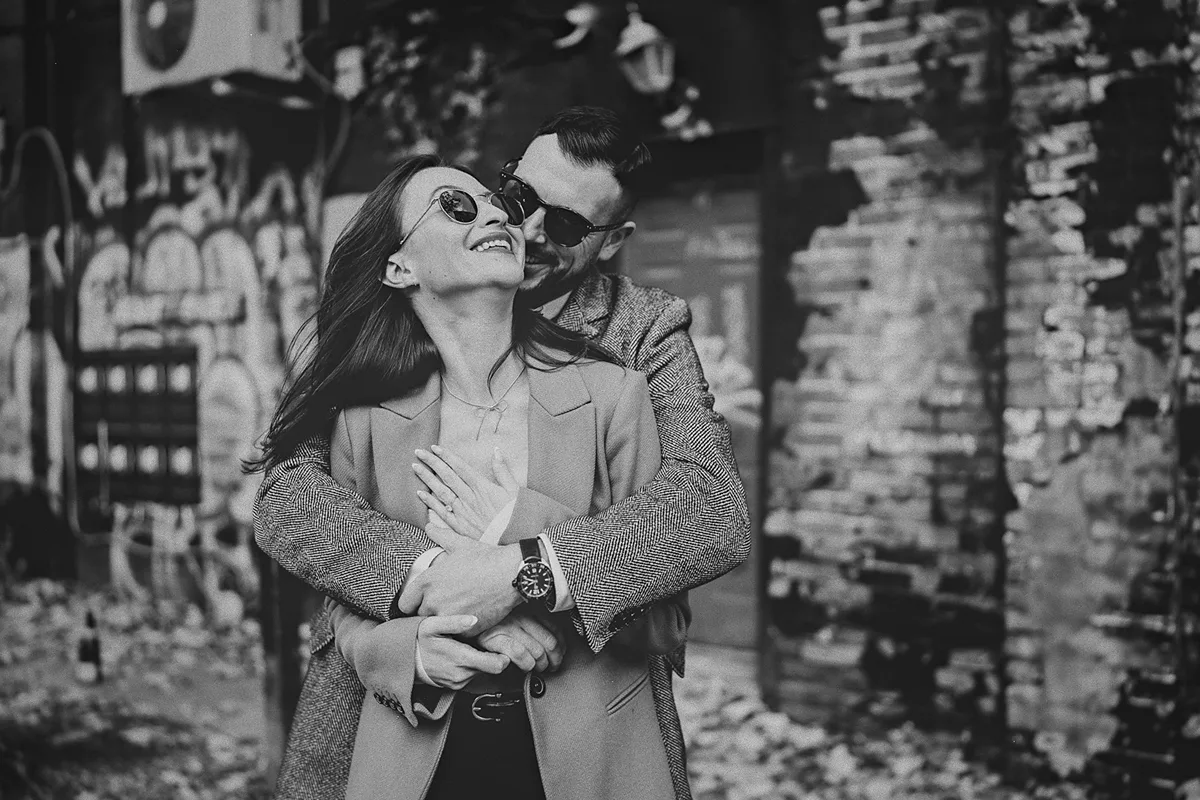 Mike embraces a joyful Roxy from behind in an urban alley.