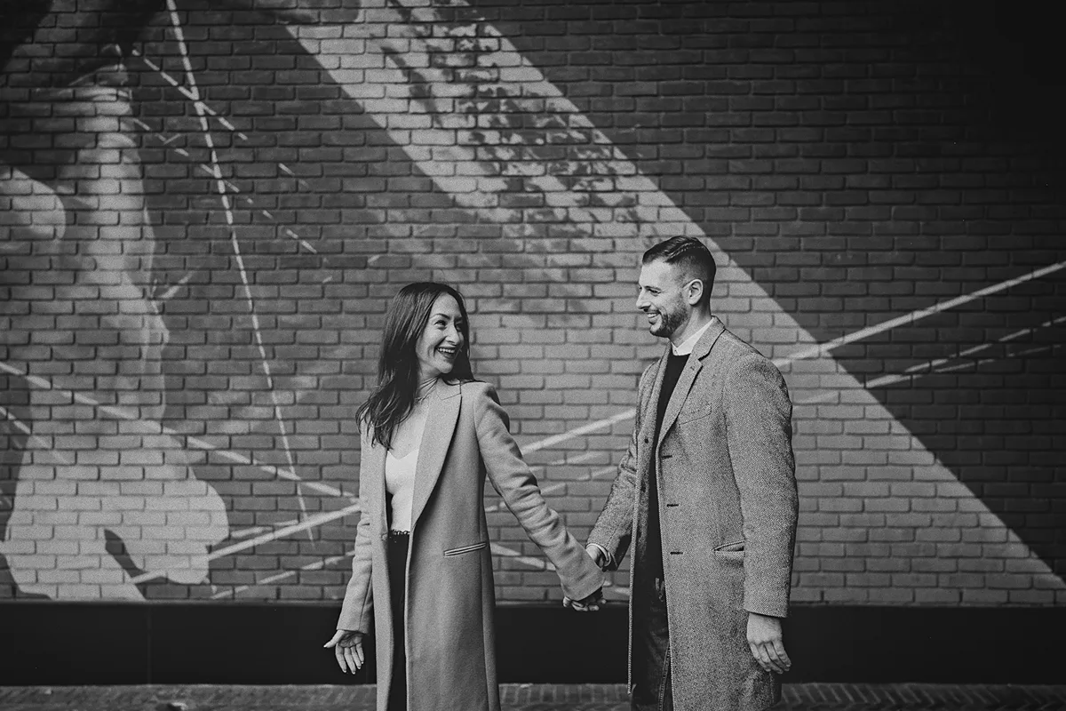 Roxy and Mike smiling at each other in front of the red wall.