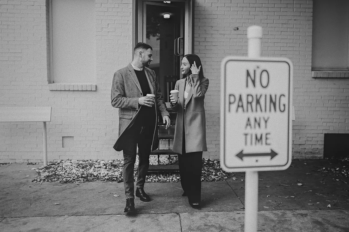 The couple leaves the cafe, laughing and holding coffee.