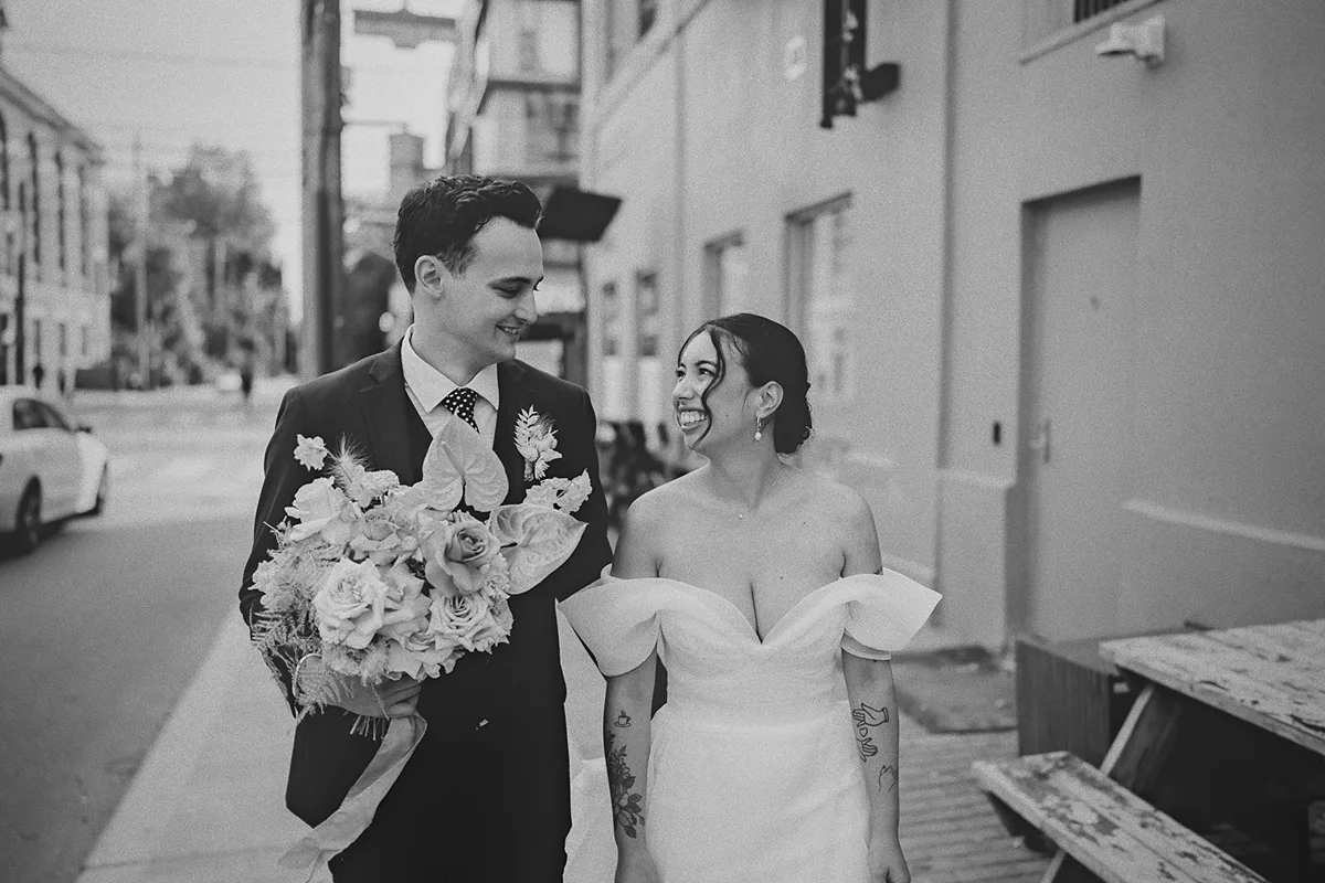 The couple walks down the sidewalk, smiling at each other.